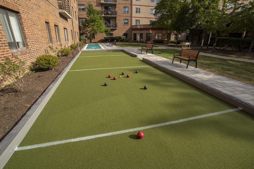 Outdoor Bocce Ball Court With Colorful Balls, Surrounded By Greenery, Benches, And A Residential Building At One Lincoln Park In Dayton.